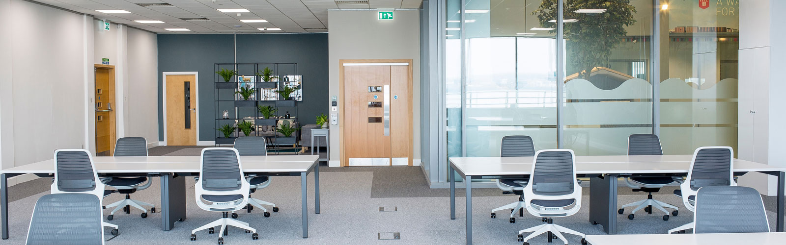 Private office with glass window in a modern open plan office with long desks and collaborative areas.