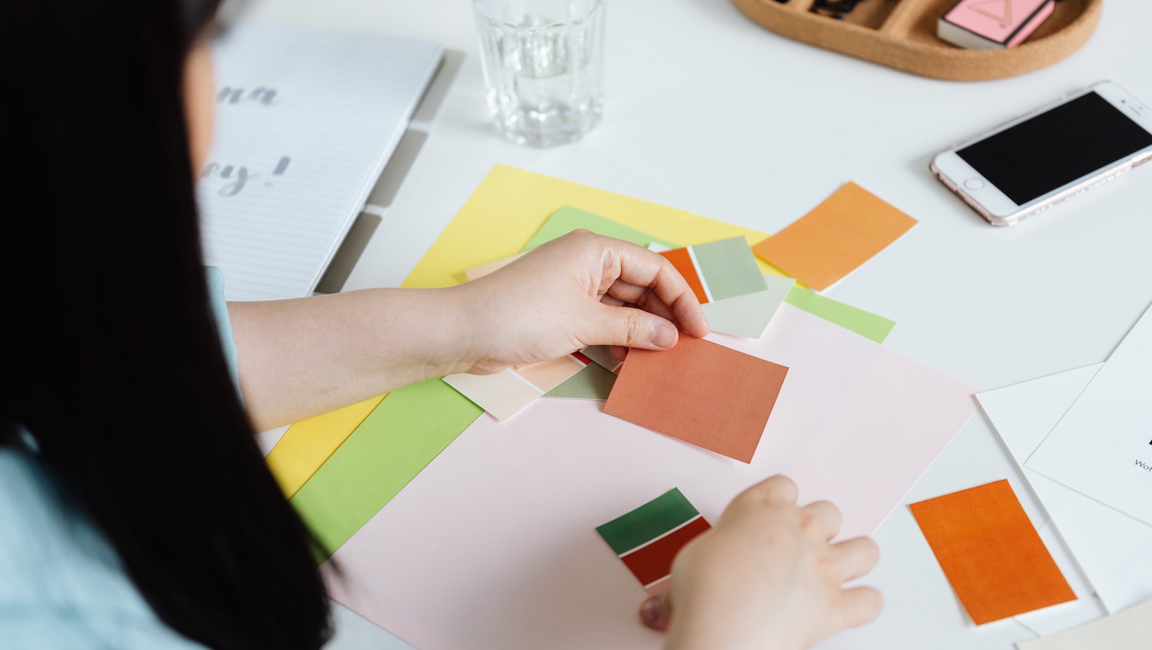 Flat lay of woman's hands sorting through fabric and paint colour swatches on a white table top