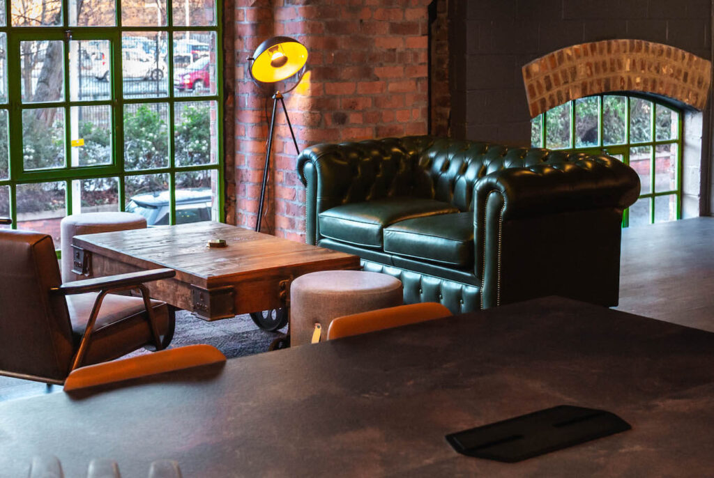 Green leather Chesterfield sofa, dark wooden coffee table and black floor lamp an industrial space with exposed