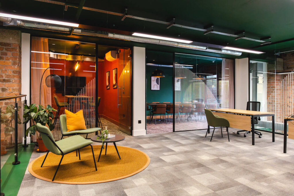 Modern office design with grey carpet tiles and muti-colured furniture on a yellow rug in front of glass diving walls