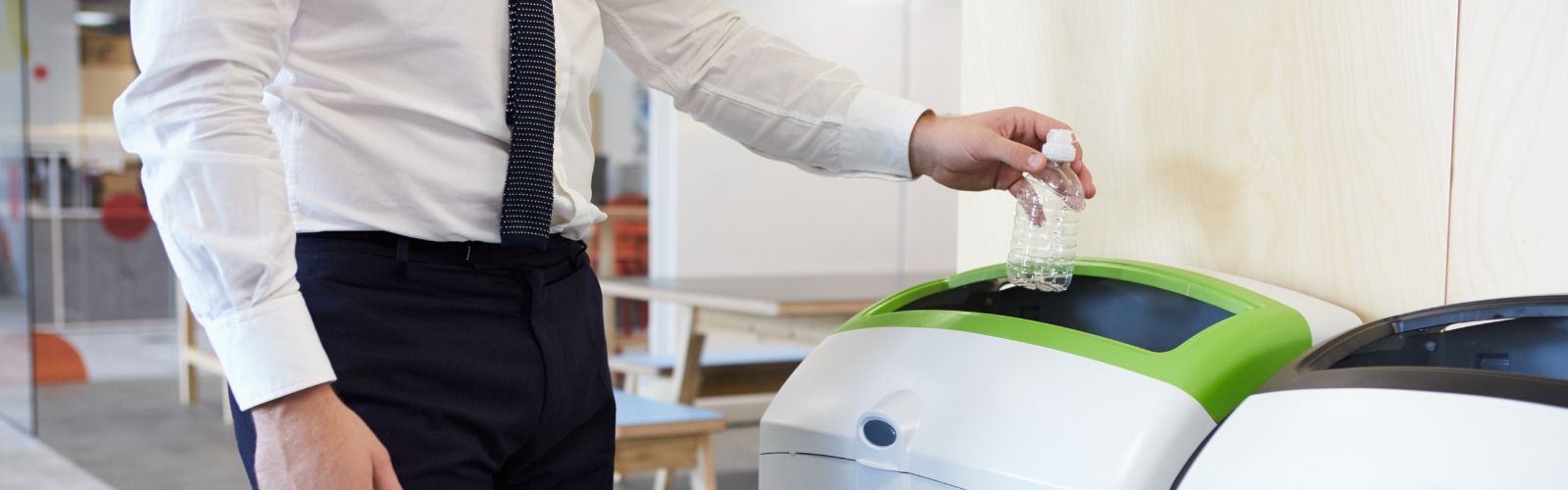 Man in office discarding plastic bottle by using recycling bin