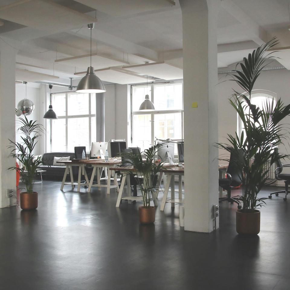 Modern office with grey floor, white pillars, indoor plants and red seats