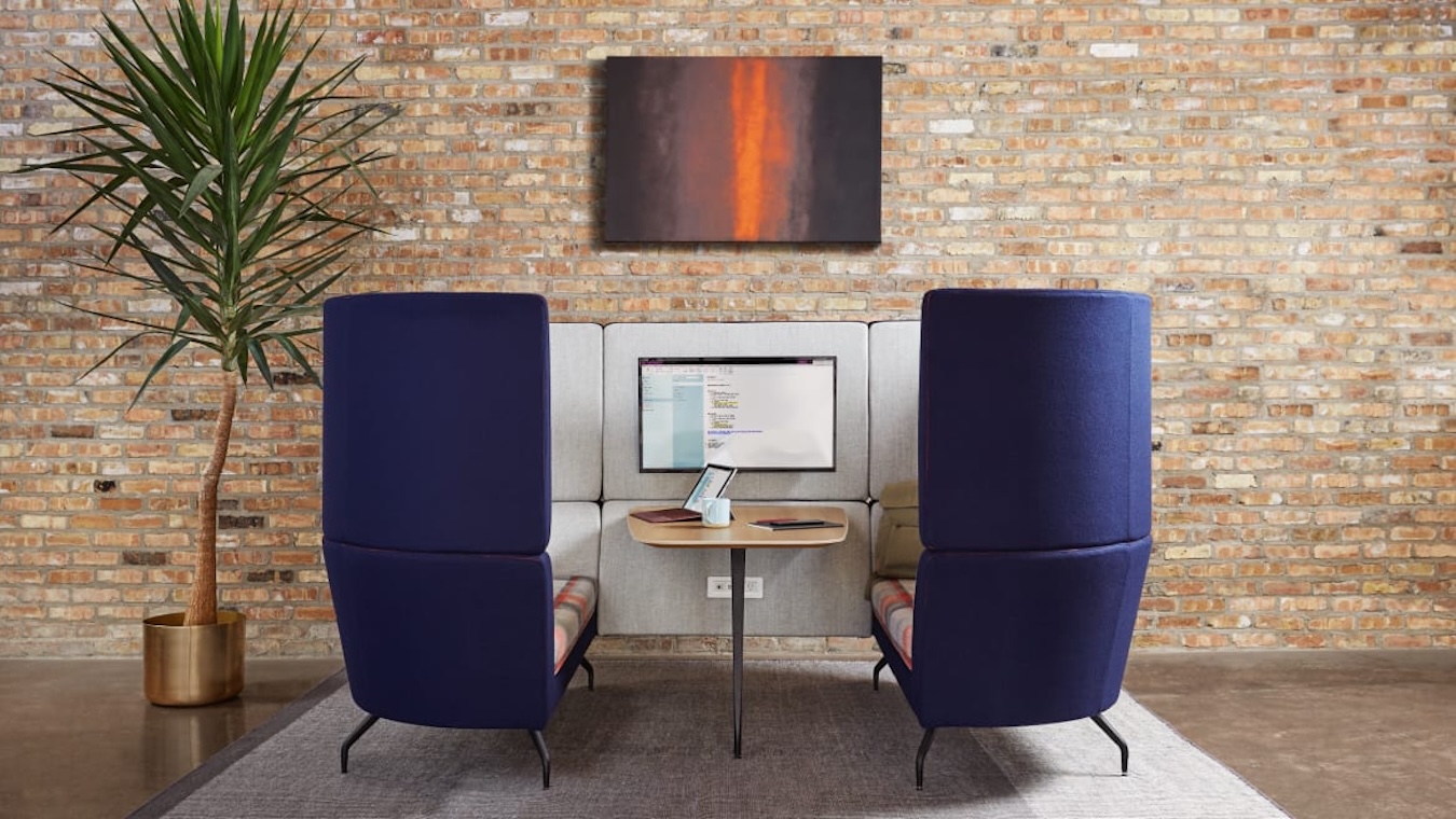 Purple and grey office booth with an integrated TV screen against a bare brick wall