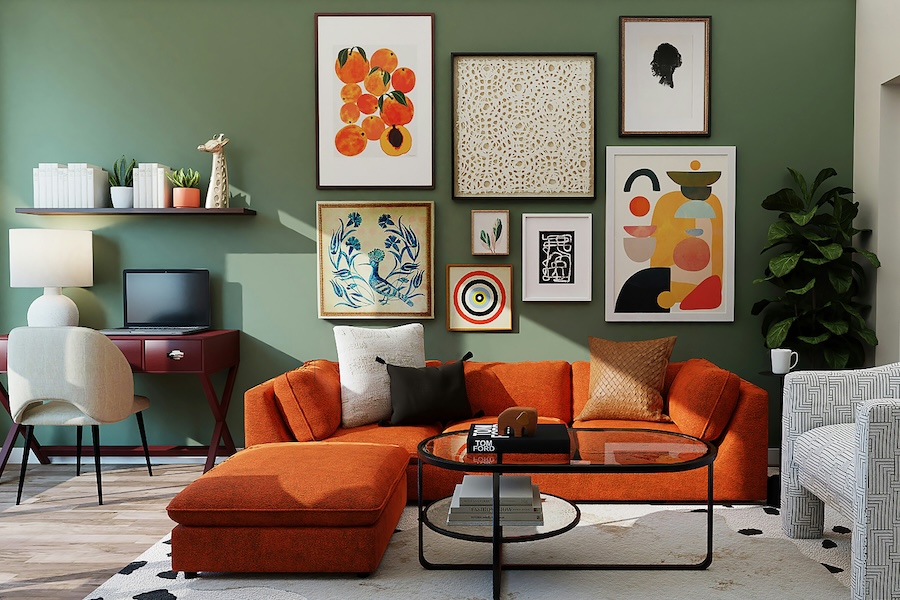 An orange sofa against a sage green wall with a collection of different size art print frames, on top of a white rug with a glass coffee table with black metal frame